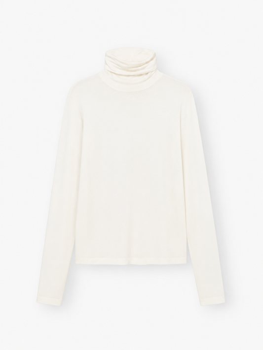 Das „Turtle Jersey White“, ein schlichter, langärmeliger, cremefarbener Rollkragenpullover, wird vor weißem Hintergrund präsentiert – ideal als weißes Jersey-Shirt für jeden Anlass. Dieses stilvolle Rollkragen-Shirt für Damen wird in Portugal meisterhaft gefertigt und verbindet Komfort mit zeitloser Eleganz.