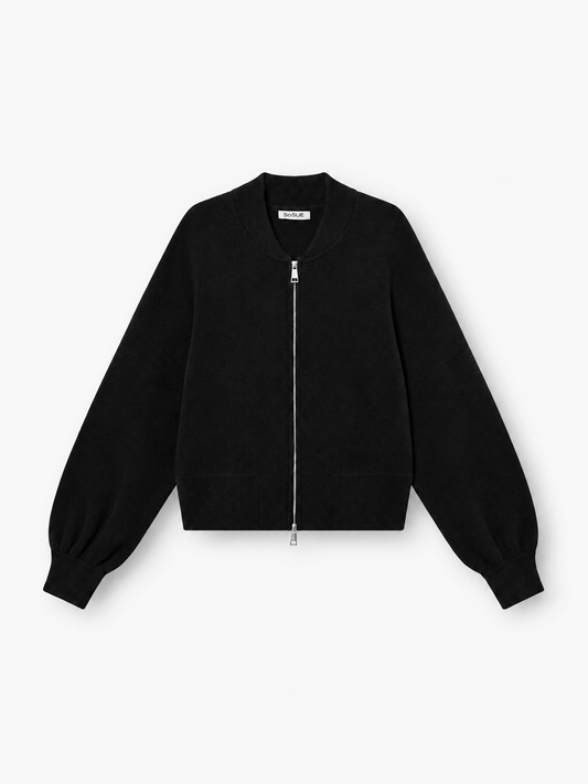 Die „Bomber Cardigan Schwarz“ ist eine Strickjacke im Bomber-Stil mit Reißverschluss, langen Ärmeln, gerippten Bündchen und einem abgerundeten Kragen – stilvoll auf weißem Hintergrund präsentiert.