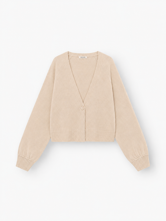 Die Antonia Short Cardigan Puder ist eine beigefarbene, langärmelige Damen-Strickjacke mit V-Ausschnitt, gerippten Bündchen und Saum sowie einem Ein-Knopf-Verschluss. Sie besteht aus einer luxuriösen Merinowolle-Kaschmir-Mischung und wird vor einem weißen Hintergrund präsentiert.